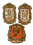 DIVERSOS, conjunto com três (3) brasões decorativos, confeccionados em resina com acabamento em tom dourado e fundo em vermelho, molduras ricamente trabalhadas em estilo clássico. Apresentam símbolos heráldicos distintos, sendo: leão rampante, castelo fortificado e elmo/capacete medieval. Leves falhas na pintura, medem 33x20cm.