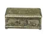 METAL PRATEADO, uma (1) caixa porta joias confeccionada em metal espessurado a prata ricamente trabalhada em alto-relevo, apresentando cena neoclássica na tampa, com figuras humanas em ambiente bucólico e arquitetônico (colunata clássica), possivelmente inspirada em temas greco-romanos. Bordas decoradas com friso contínuo ornamentado, laterais com molduras em relevo e motivos florais em destaque, leves mossas e falhas no banho, medindo 5,5x12x7,5cm.