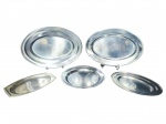 METAL PRATEADO INOX, cinco (5) travessas confeccionadas em aço inox de tamanhos distintos, sendo 4 ovais, maior medindo 36,5x26cm e menor 24,5x15cm (pequena mossa na alça) e 1 redonda, medindo 24cm. Apresentam marcas de uso.