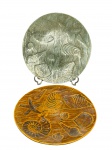 CERÂMICAS, dois (2) pratos decorativos confeccionados em cerâmica vitrificada nas tonalidades verde e marrom, moldado por conchas marítimas distintas e ondualações, medindo 23cm. Ambos assinados no verso.