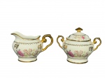 PORCELANA REAL, lote com duas (2) peças confeccionadas em porcelana nacional na tonalidade branca com pintura de flores e folhagens em policromia, adornada por guirlandae elementos florais em vasta douração, sendo: A) 1 leiteira, medindo 9x14x7cm e B) 1 açucareiro, medindo 11x14,5x8cm.