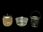VIDROS, lote com três (3) peças confeccionadas em vidro, sendo: A) 1 biscoiteira revestida em malha de metal dourado, borda prateada com falhas na douração e tampa plástica, medindo 15x10cm, B) 1 balde para gelo confeccionado em vidro fumê com moldagem em dedão, galeria e alça em metal prateado, apresenta leves mossas, medindo 12x12cm e C) 1 bomboniere confeccionada em vidro translucido com lapidação de frisos, folhagens e esferas em baixo relevo, medindo 12x17cm, leves bicados na borda.