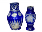 CRISTAL DOUBLE, dois (2) vasos confeccionados em CRISTAL DOUBLE na tonalidade azul, lapidado por palmas e elementos geométricos em baixo relevo, 1 necessita relapidar a borda e possui bicados na base, medindo 12cm e menor 10,5cm.