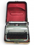 DIVERSOS, uma (1) máquina de escrever da marca Remington, modelo portátil, acompanhada de estojo rígido original, com interior revestido em material acolchoado na cor vermelha, corpo metálico em acabamento claro, teclado completo, barras de tipos aparentes e componentes mecânicos visíveis, característica das máquinas portáteis produzidas em meados do século XX. Peça de reconhecida importância histórica no desenvolvimento da escrita mecânica e da comunicação impressa, apresenta sinais de uso e oxidações, possui dano no estojo, vide foto, medindo 17,5x35x36cm.