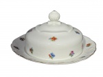 KPM Krister Porzellan-Manufaktur (Fundada em 1831 por Carl Franz Krister), uma (1) manteigueira confeccionada em porcelana na tonalidade branca, elementos vegetalistas em relevo na pasta, pintura de flores e folhagens em policromia e borda filetada em ouro, medindo 10x19cm, apresenta leves falhas na douração.