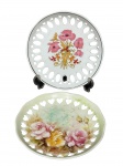PORCELANAS, dois (2) pratos decorativos confeccionados em porcelana na tonalidade branca com borda em vazados, ambas decoradas por elementos florais em policromia, medindo 19cm e 18cm.