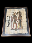 QUADRO, uma (1) reprodução em papiro, representando cena de inspiração egípcia, com figuras em posição frontal, trajes tradicionais e escrita hieroglífica na composição, moldura em metal fosco com proteção em vidro, medindo 51x41cm.