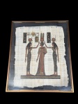 QUADRO, uma (1) reprodução em papiro, representando cena de inspiração egípcia, com figuras femininas em posição frontal, portando símbolos tradicionais, acompanhadas de escrita hieroglífica, moldura em metal de tom escuro com proteção em vidro, medindo 49,5x41cm.