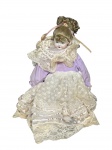 COLECIONISMO, uma (1) boneca de coleção com cabeça, pés e mãos em biscuit, corpo em pano, vestes na tonalidade lilás com rendas brancas, rosto pintado a mão, medindo 47cm de altura.