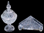 CRISTAIS, lote com duas (2) peças confeccionadas em cristal translucido, sendo: A) 1 compoteira, lapidada por palmas, bico de jaca, esferas e elementos geométricos em baixo relevo, medindo 22x11cm e B) 1 porta guardanapos com lapidação de palmas, elementos geométricos e dedões na borda em baixo relevo, medindo 10,5x17,5x4cm.