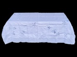 CAMA, MESA & BANHO, uma (1) toalha de mesa quadrada confeccionada em tecido branco com bordados manuais em relevo, apresentando motivos florais estilizados distribuídos pelo campo da peça, medindo 150x150cm.
