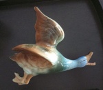 Escultura em porcelana vitrificada e policromada representando pato em voo medindo 28 cm por 26 cm por 11 cm, apresenta colagem no bico.