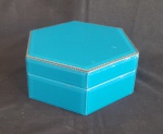 Caixa porta joias sextavada em madeira revestida de placas de vidro bisotado e pintado de azul turquesa na parte posterior, faixa perolada em metal na aresta e interior forrado de veludo negro. Alt. 8 x diam. 20cm. Em bom estado de conservação.