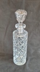 Garrafa em cristal formato cilíndrico tampa adaptada,apresenta trincado na base medindo 27 cm de altura por 9 cm de diâmetro..