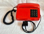 Telefone Ericson em baquelit vermelho medindo 10 cm por 21 cm por 17 cm, possui placa de inventário da antiga TV Record.