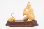 Escultura de marfim oriental representando encantador de serpente sobre base de madeira oval. Medida da base: cm. Altura total:  cm.