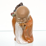 Escultura em porcelana esmaltada representando Shoulao (Shouxing), divindade chinesa associada à longevidade e à sabedoria no taoismo. A figura apresenta crânio proeminente e testa elevada, barba longa e branca bipartida, traços iconográficos característicos do personagem. Veste túnica longa, com policromia em tons de azul, ocre e branco. Na mão direita segura o pêssego da longevidade, atributo simbólico da imortalidade, enquanto ao ombro observa-se cabaça ritual, associada ao elixir da vida. Base integrada à modelagem, com abertura inferior circular e marca incisa na pasta. Peça moldada em porcelana, com esmaltação vítrea e acabamento manual. Apresenta desgaste compatível com o uso e a idade, além de ausência de elemento originalmente aplicado na mão direita (não estrutural), conforme observado. Produção chinesa, século XX. Medidas: Alt.: 9,5 x Comp.: 6 x Larg.: 6,5 cm.