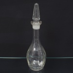 Garrafa em vidro incolor, moldada, constituída por bojo globular, base circular plana e fundo espesso. Região inferior apresenta ressaltos prismáticos verticais em disposição radial. Gargalo troncocônico alongado, dotado de borda circular lapidada com superfície fosca destinada à vedação por atrito. Acompanha rolha maciça, também troncocônica, provida de caneluras longitudinais e encaixe lapidado compatível. Apresenta um trincado na parte superior do gargalo visível nas fotos. Medidas: Alt.: 38,5 x Diam.: 11,5 cm.