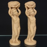 Par de esculturas representando putti em função de cariátide, moldados em executados em resina de tonalidade marfim. Apresentam postura em contrapposto, com membros superiores elevados sustentando cestos florais, ornamentados por elementos vegetais em relevo, exibem panejamento curto, com tratamento contínuo do dorso integrado ao suporte vertical, formando eixo estrutural único entre base e atributo superior; base circular, planas, moldadas no mesmo material. Medidas: Alt.: 24 x Diam.: 6 cm.