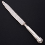 Christofle, Paris - França(Fundada em 1830 por Charles Christofle). Luxuosa faca trinchante confeccionada em metal espessurado à prata, fabricação francesa do início do século XX, executada ao estilo do período Louis Philippe. Padrão "Chinon", usado a partir de 1862, conhecido anteriormente como "filet" ou "vieux Paris". Cabo apresenta "ombros" e margem contornada por frisos de terminação cordiforme sobre extremo arredondado. Lâminas em aço marcada CHRISTOFLE A PARIS(apresentam sinais de oxidação). Marca da manufatura puncionada no verso do cabo. Med.: Comp. 32 cm.