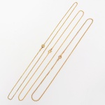 Três(03) correntes em metal banhado à ouro, constituídas por elos articulados, formando malha contínua de perfil linear e seção regular. Dois exemplares executados em malha veneziana, composta por elos quadrangulares justapostos; um em malha tipo cadeado, formada por elos ovais alongados interligados. Todas com fecho tipo bóia, acionado por mecanismo de mola, associado a argola terminal fechada. Medidas: Comp.: 21 cm; Comp.: 23 cm; Comp.: 25 cm.