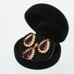 Conjunto composto por par de brincos e pingente, confeccionados em metal dourado, estruturados por base fundida e acabamento polido, apresentam pino reto posterior com sistema de pressão, montados sobre suporte circular, e corpo frontal em forma de gota, com gema(natureza não testada) central lapidada com mesmo formato fixada em engaste por garras, moldura periférica é composta por pedras incolores lapidação brilhante, dispostas radialmente em engastes individuais, formando contorno contínuo; pingente repete a mesma composição formal, com gema central lapidação gota em engaste por garras, circundada por pedras incolores lapidação brilhante, fixadas em engaste fechado, com argola superior integrada para suspensão. Verso dos elementos com estrutura vazada, trabalho em relevo radial e marcação de manufatura ilegível, vide fotos. Acondicionadas em estojo. Medidas: 2 x 1,5 cm; Pingente: 2,5 x 1,5 cm.