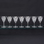 Exuberante conjunto de taças de pé alto, para vinho branco, em cristal europeu, provavelmente   tcheco, diáfano e incolor. Bojo obcônico, profusamente talhado com padrão de folhas estilizadas, estrelas e formas geométricas em relevo, organizado em painéis verticais facetados, fuste longo de seção hexagonal, base circular, fundo com lapidação radial em estrela, com raios  partindo do centro em disposição simétrica. Composto de sete(07) unidades. Medidas: Alt.: 18 x Diam.: 10 cm.