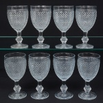 Elegante conjunto de taças de pé alto, vinho branco, em vidro prensado, diáfano e incolor; bojo oval moldado com sucessão de lonsagos relevados, padrão dito "bico de jaca", fuste haxagonal com anel intermediário, base circular de fundo estrelado. Composto de oito(08) unidades. Medidas: Alt.: 15,5 x Diam.: 8 cm.