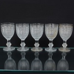 Elegante conjunto de taças de pé alto, para vinho tinto, em vidro prensado, diáfano e incolor; bojo oval moldado com sucessão de lonsagos relevados, padrão dito "bico de jaca", fuste haxagonal com anel intermediário, base circular de fundo estrelado. Composto de cinco(05) unidades. Medidas: Alt.: 14 x Diam.: 6,5 cm.