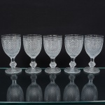 Elegante conjunto de taças de pé alto, para vinho tinto, em vidro prensado, diáfano e incolor; bojo oval moldado com sucessão de lonsagos relevados, padrão dito "bico de jaca", fuste haxagonal com anel intermediário, base circular de fundo estrelado. Composto de cinco(05) unidades. Medidas: Alt.: 14 x Diam.: 6,5 cm.