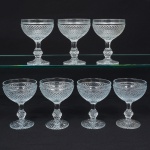 Elegante conjunto de taças de pé alto, para champanhe, em vidro prensado, diáfano e incolor; bojo hemisférico moldado com sucessão de lonsagos relevados, padrão dito "bico de jaca", fuste haxagonal com anel intermediário, base circular de fundo estrelado. Composto de sete(07) unidades. Medidas: Alt.: 13 x Diam.: 9,5 cm.