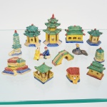 Conjunto de miniaturas arquitetônicas e figuras em porcelana chinesa policromada, representando edificações e elementos arquitetônicos de inspiração chinesa, incluindo pagodes de múltiplos pavimentos, pavilhões com telhados escalonados, torres, portais e construções muradas, além de figuras humanas em escala compatível, dispostas como cena urbana ou paisagística, apresentam telhados de cumeeira elevada, com beirais recurvos, elementos sobrepostos, bases escalonadas e volumetria modular, com decoração aplicada por pintura vitrificada nas cores verde, amarelo, azul, vermelho e branco. As figuras humanas encontram-se em posições estáticas, associadas ao conjunto arquitetônico. Executada por moldagem, com pintura manual posterior. Ausência de marca de manufatura. Composto de treze(13) unidades. Apresentam pequenos desgastes e/ou ínfimos bicados. Medidas: Alt.: 2,5 x Comp.: 3,5 x Larg.: 1 cm(2); Alt. 2 x Comp.: 2 x Larg.: 2 cm; Alt. 2 x Comp.: 4,5 x Larg. 1 cm; Alt.: 3 x Diam.: 2 cm; Alt.: 5,5 x Comp.: 2 x Larg.: 2,5 cm; Alt. 3 x Comp.: 2,3 x Larg.: 2,3 cm; Alt.: 2,6 x Comp.: 2,5 x Larg.: 2 cm. Alt.: 2,5 x Comp.: 5 x Larg.: 2,5 cm; Alt.: 3,5 x Comp.: 3,5 x Larg.: 3 cm; Alt.: 4,5 x Comp.: 3,5 x Larg.: 3,5 cm; Alt.: 4 x Comp.: 4 x Larg.: 3 cm; Alt.: 7 x Comp. 4 x Larg.: 4 cm.