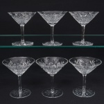 Exuberante conjunto de taças de pé alto, para champanhe, em cristal europeu, provavelmente   tcheco, diáfano e incolor. Bojo obcônico, profusamente talhado com padrão de folhas estilizadas, estrelas e formas geométricas em relevo, organizado em painéis verticais facetados, fuste longo de seção hexagonal, base circular, fundo com lapidação radial em estrela, com raios  partindo do centro em disposição simétrica. Composto de seis(06) unidades. Medidas: Alt.: 12,5 x Diam.: 11,5 cm.
