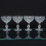 Elegante conjunto de taças de pé alto, para champanhe, em vidro prensado, diáfano e incolor; bojo hemisférico moldado com sucessão de lonsagos relevados, padrão dito "bico de jaca", fuste haxagonal com anel intermediário, base circular de fundo estrelado. Composto de quatro(04) unidades. Medidas: Alt.: 13 x Diam.: 9,5 cm.