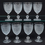 Elegante conjunto de taças de pé alto, vinho branco, em vidro prensado, diáfano e incolor; bojo oval moldado com sucessão de lonsagos relevados, padrão dito "bico de jaca", fuste haxagonal com anel intermediário, base circular de fundo estrelado. Composto de oito(08) unidades. Medidas: Alt.: 15,5 x Diam.: 8 cm.