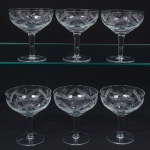 Conjunto de taças para champanhe em meio cristal, diáfano e incolor, bojo hemisférico talhado com frisos diagonais e flores estilzadas, fuste tubular sobre base circular. Composto de cinco(05) unidades. Medidas: Alt.: 11 x Diam.: 9,5 cm.