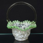 Cesto decorativo em vidro soprado, Europa Central (Boêmia), final do século XIX / início do século XX. Corpo em vidro translúcido com aplicação de inclusões irregulares de tonalidade branco opaco (spatter glass), bojo de forma campanular. Borda recortada e ondulada, com filete aplicado em vidro verde translúcido. Alça aplicada a quente, em arco contínuo, seção circular. Base plana. Medidas: Alt.: 17,5 x Comp.: 15 x Larg.: 14 cm.