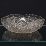 Fruteira executada em meio cristal prensado, diáfano e incolor, formato quadrangular de quinas arredondadas, borda revirada para cima, ondulada e recortada em arcos, verso ricamente relevado com composição geométrica, composta por sucessão de hexagonos, encimados por palmetas. Medidas: Alt.: 7 x Comp.: 19,5 x Larg.: 19,5 cm.