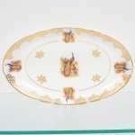 Porcelana Real, Mauá - SP(Fundada em 1943 por Fritz Erwin Schmidt). Belíssima travessa oval em porcelana nacional da década de 1950/60. Esmaltagem vítrea na cor branca, decoração composta por cena central com casal de pavões, pousados entre ramos, flores e folhagens, executada em estampagem policromada; orla ornada por motivos fitomórficos e treliçados em douradura, distrubuídos em reservas, com friso circular interno e filete contínuo acompanhando o contorno da borda.  Medida: Comp.: 29,5 x Larg.: 17,5 cm.
