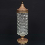 Compoteira executada em vidro prensado, incolor, corpo cilíndrico moldado com comosição geométrica em relevo losangular contínuo, tampa campaniforme encimada por puxador com feitio de pináculo e base circular elevada em metal. Necessita refazer banho de prata. Medidas: