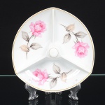 Petisqueira em porcelana nacional da década de 1950/60, esmaltagem vítrea na cor branca, de formato triangular com cantos arredondados, dividido internamente em três compartimentos, pegador central cilíndrico,borda com filete dourado aplicado. Decoração policromada com flores distribuídas em cada compartimento, predominando as tonalidades rosa e grisaile. Marca da manufatura no verso. Medidas: Alt.: x Diam.: