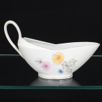 Porcelana Real, Mauá - SP(Fundada em 1943 por Fritz Erwin Schmidt). Elegante molheira navicular em porcelana nacional da década de 1960, estilo Art Déco; esmaltagem vítrea na cor branca, decoração aplicada por estampagem policromada, com motivos florais estilizados compostos por flores radiais em tons de rosa e amarelo, acompanhadas por folhas em grisaille, distribuídos no corpo, filetes dourados aplicados na borda superior do corpo e na base, alça lateral curvada. Marca da manufatura no verso. Medidas: Alt.: x Comp.: x Larg.: