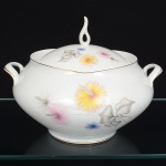 Porcelana Real, Mauá - SP(Fundada em 1943 por Fritz Erwin Schmidt). Sopeira em porcelana nacional da década de 1960, esmaltagem vítrea na cor branca, corpo bojudo assentado sobre base circular, decoração aplicada por estampagem policromada, com motivos florais estilizados compostos por flores radiais em tons de rosa e amarelo, acompanhadas por folhas em grisaille, distribuídos no corpo e na tampa, tampa abaulada com pega vazada elevada, moldada na própria porcelana, filetes dourados aplicados na borda superior do corpo e na aba da tampa, alças laterais em "C" reviradas para cima. Marca da manufatura no verso. Medidas: Alt.: x Comp.: x Larg.: