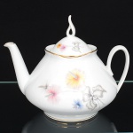 Porcelana Real, Mauá - SP(Fundada em 1943 por Fritz Erwin Schmidt). Bule para chá em porcelana nacional da década de 1960, esmaltagem vítrea na cor branca, corpo bojudo de formato cônico assentado sobre base circular, decoração aplicada por estampagem policromada, com motivos florais estilizados compostos por flores radiais em tons de rosa e amarelo, acompanhadas por folhas em grisaille, distribuídos no corpo e na tampa, tampa abaulada com pega vazada elevada, moldada na própria porcelana, filetes dourados aplicados na borda superior do corpo e na aba da tampa, alça lateral curvada, bico vertedor rtilíneo de seção tubular. Marca da manufatura no verso. Medidas: Alt.: x Comp.: x Larg.: