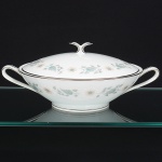 NORITAKE, Nagoya - Japão(Fundada em 1904 pelos irmãos Ichizaemon e Toyo Morimura). Elegante terrina coberta para vegetais em porcelana japonesa da década de 1960/70. Padrão 'WELLESLEY 6214', produzido entre os anos de 1961 a 1976. Esmaltagem vítrea na cor branca, decorada com delicado padrão floral com flores brancas, folhas em suave tons de verde e outros tons pastéis, bordas contornadas por friso em platina, bojo hemisférico sobre base circular, tampa abaulada encimada por puxador em dupla folhagem estilizada, alças laterais curvadas. Marca da manufatura no verso. Med.: Alt. 13 x Comp. 28,5 x Larg. 22 cm.