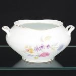 Porcelana Real, Mauá - SP(Fundada em 1943 por Fritz Erwin Schmidt). Sopeira sem tampa em porcelana nacional da década de 1960, estilo Art Déco; esmaltagem vítrea na cor branca, decoração aplicada por estampagem policromada, com motivos florais estilizados compostos por flores em tons de rosa, azul, verde, violeta e amarelo, distribuídos no corpo, filetes dourados aplicados na borda superior do corpo e na base, alça lateral em "C" revirado para cima. Marca da manufatura no verso. Medidas: Alt.: x Comp.: x Larg.:
