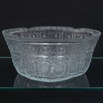 Grande fruteira executada em cristal espesso, diáfano e incolor, com paredes ligeiramente divergentes e borda superior serrilhada por lapidação regular. Decoração integral obtida por lapidação geométrica profunda, composta por painéis verticais com motivos de estrelas radiadas, losangos, traços cruzados e cartelas ovais com fundo pontilhado, fundo lapidado com composição geométrica centralizada, formada por quadrículas e estrelas sobrepostas, visível tanto pelo interior quanto pela base. Medidas: Alt.: 12 x Comp.: 27,5 x Larg.: 20 cm.