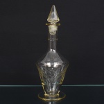 Garrafa executada em vidro, translúcido e incolor, bojo losangular assentado sobre base circular, lavrado com painéis simétricos, com motivos estrelados e elementos lineares, gargalo tubular, tampa de seção cônica. Medidas: