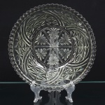 Bowl executado em meio cristal prensado, formato hemisférico, com borda recortada em gomos regulares, decoração composta por motivos geométricos organizados em campos radiais, fundo com medalhão central circular, decorado por roseta estrelada de múltiplas pontas, subdividida em quatro quadrantes com motivos florais estilizados, área intermediária com faixas curvas entrelaçadas, intercaladas por estrelas facetadas e malha geométrica em losangos, corpo moldado com padrões triangulares e estrelados, formando composição contínua ao redor da peça. Medidas: Alt.: 8 x Diam.: 27 cm.