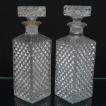 Duas(02) garrafas para uísque em vidro prensado, translúcido e incolor, corpo quadrangular ricamente moldado com losangos em relevo, tampa achatada, ombro trapezoidal, gargalo circular, borda recortada, fundo estrelado. Med.: Alt. 25 x Comp. 8 x Larg. 8 cm.